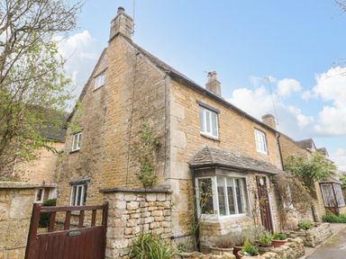 A stone cottage with a wooden gate and potted plants outside at Tuesday Cottage in Bourton-On-The-Water