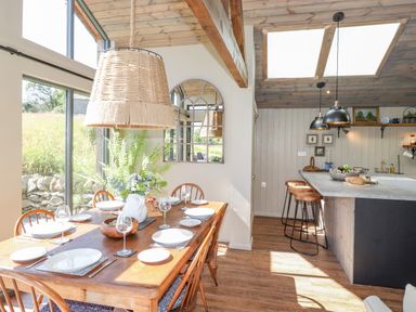 A dining area with a wooden table set for six and a kitchen island with stools under skylights at The Owl's Shack in Kendal