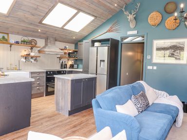 A kitchen with wooden cabinets, island, stainless steel refrigerator, stove, and a blue couch with cushions at The Owl's Shack in Kendal