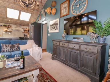 A living room with a blue sofa a wooden coffee table a large wall clock and a wooden sideboard at The Owl's Shack in Kendal