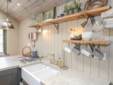 A kitchen corner with a double sink brass faucet shelves with cups bowls and plants at The Owl's Shack in Kendal