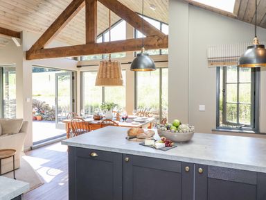 A kitchen island with bread cheese and fruit bowl near a dining table with chairs and pendant lights at The Owl's Shack in Kendal