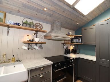 A kitchen with a sink black stove wooden shelves and gray cabinets at The Owl's Shack in Kendal