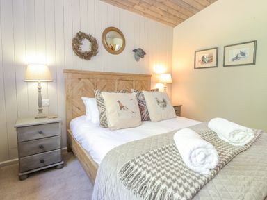 A bedroom with a wooden bed frame two bedside tables with lamps and decorative pillows at The Owl's Shack in Kendal