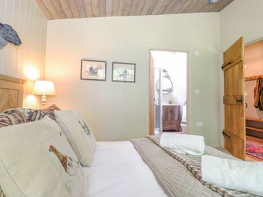 A bedroom with a bed pillows lamps and an open door leading to a bathroom at The Owl's Shack in Kendal