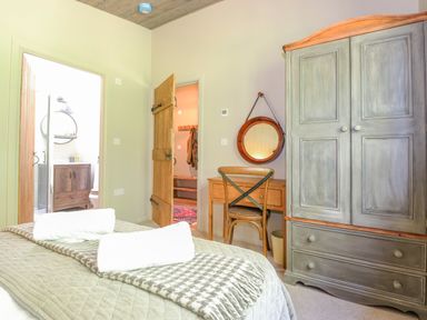 A bedroom with a bed, a wooden wardrobe, a wooden desk with a chair, and a round mirror at The Owl's Shack in Kendal