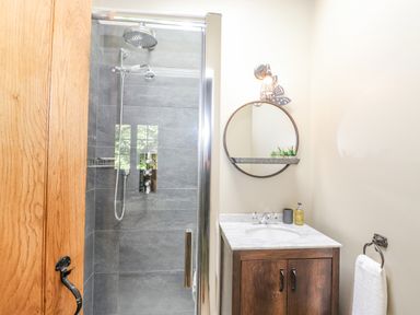 A bathroom with a shower area and a wooden vanity with a round mirror above at The Owl's Shack in Kendal