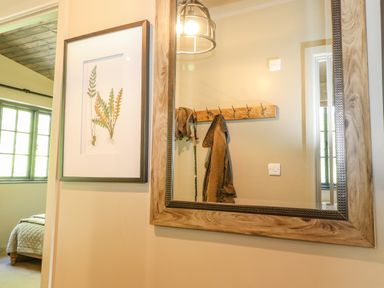 A hallway with a large wooden framed mirror and a framed botanical print with a bedroom visible through the doorway at The Owl's Shack in Kendal