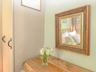 A wooden dresser with a vase of white flowers and a decorative framed mirror reflecting a bed at The Owl's Shack in Kendal