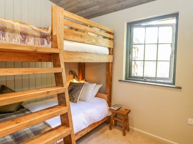 A bedroom with wooden bunk beds and a small wooden stool by a window at The Owl's Shack in Kendal