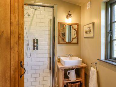 A bathroom with a wooden door a glass shower enclosure a wooden sink vanity with a white basin a mirror and a window at The Owl's Shack in Kendal