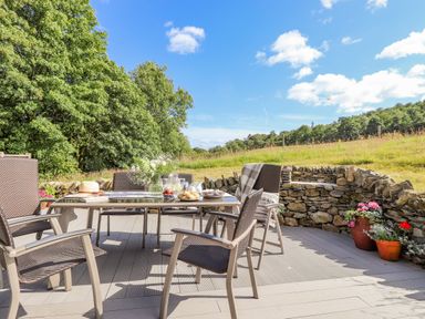 An outdoor patio with a dining table and chairs with food and drink set on the table and a stone wall and grassy field in the background at The Owl's Shack in Kendal