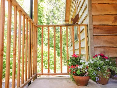 A wooden porch with flower pots containing red white and purple flowers at The Owl's Shack in Kendal