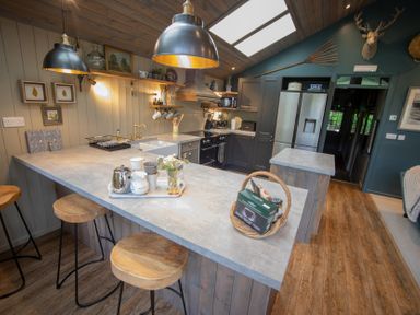 A kitchen with a countertop bar with stools pendant lights and a refrigerator at The Owl's Shack in Kendal