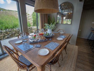 A dining room with a wooden table set with plates glasses bread and flowers at The Owl's Shack in Kendal