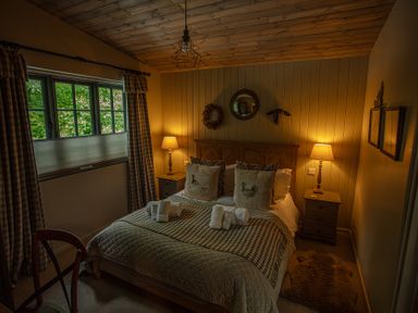 A bedroom with a double bed two bedside tables with lamps checkered curtains and a small window at The Owl's Shack in Kendal