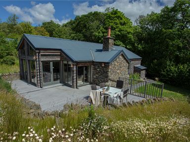 A stone and wood house with a patio table and chairs in a garden at The Owl's Shack in Kendal