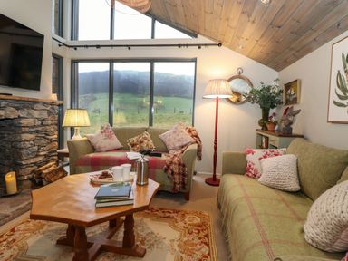 A living room with sofas pillows a wooden coffee table and large windows showing a grassy landscape at The Badger's Shack in Garnett Bridge Longsleddale Near Kendal