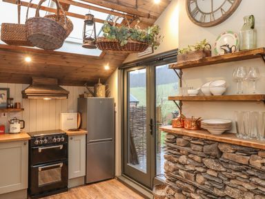 A kitchen with a stove fridge hanging baskets and shelves with dishes at The Badger's Shack in Garnett Bridge Longsleddale Near Kendal
