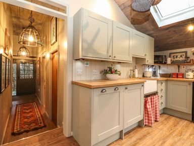 A kitchen with light cabinets wooden countertops a farmhouse sink and a hallway with hanging lights and a patterned rug at The Badgers Shack in Garnett Bridge Longsleddale Near Kendal