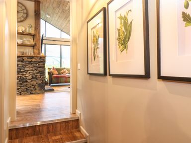A hallway with framed botanical prints on the wall leading to a living room with a stone fireplace and a sofa at The Badgers Shack in Garnett Bridge Longsleddale Near Kendal