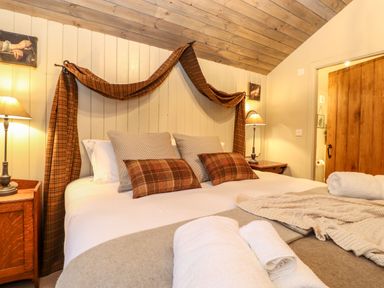A bedroom with a wooden ceiling a bed with pillows and blankets bedside tables with lamps and an open wooden door at The Badger's Shack in Garnett Bridge Longsleddale Near Kendal