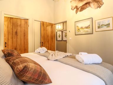 A bedroom with a bed pillows towels on the blanket wooden doors landscape paintings and animal fur on the wall at The Badger's Shack in Garnett Bridge Longsleddale Near Kendal