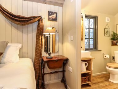A bedroom with a bed pillow side table and lamp next to a bathroom with a toilet sink and window at The Badger's Shack in Garnett Bridge Longsleddale Near Kendal