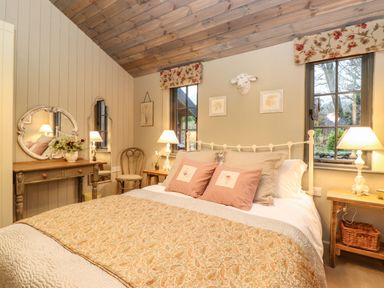 A bedroom with a double bed bedside tables lamps wooden ceiling and floral decor at The Badgers Shack Garnett Bridge Longsleddale Near Kendal