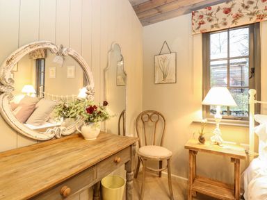 A bedroom corner with a wooden dressing table with a flower vase a wooden chair a side table with a lamp and a window at The Badger's Shack in Garnett Bridge Longsleddale Near Kendal