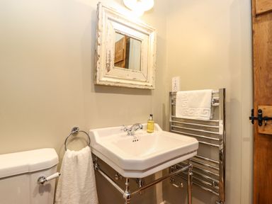 A bathroom with a white sink, a mirror with a distressed white frame, a toilet, and a towel rack with towels at The Badger's Shack in Garnett Bridge Longsleddale Near Kendal