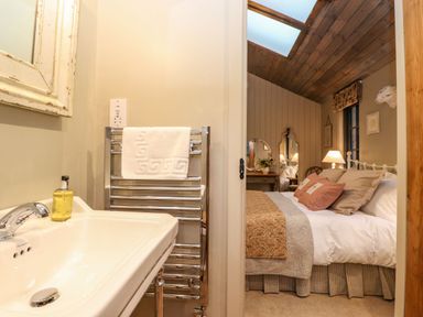 A bathroom sink with soap and towel rail next to a bedroom with bed and bedside lamps at The Badger's Shack in Garnett Bridge Longsleddale Near Kendal