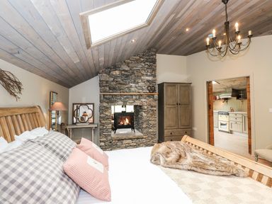 A bedroom with a wooden bed frame stone fireplace and a view into a kitchen at The Hare's Shack in Garnett Bridge Longsleddale Near Kendal