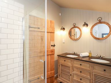 A bathroom with two sinks double mirrors wooden vanity and a glass shower enclosure at The Hare's Shack in Garnett Bridge Longsleddale Near Kendal