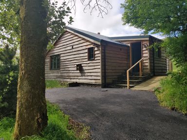 A wooden cabin with stone steps and a handrail at the entrance surrounded by trees and greenery at The Hare's Shack in Garnett Bridge Longsleddale Near Kendal