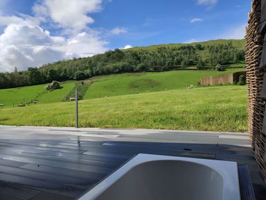 An outdoor bathtub on a wooden deck facing green hills with grass trees and sheep at The Hare's Shack in Garnett Bridge Longsleddale Near Kendal