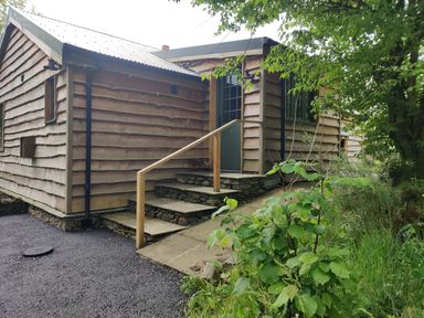 Outside view of a wooden cabin with stone steps leading to a door surrounded by greenery at The Hare's Shack in Garnett Bridge Longsleddale Near Kendal