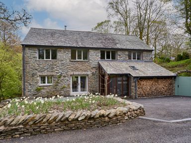 A stone house with a slate roof and a front garden with flowers at The Old Water Mill in Kendal