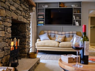 A living room with a stone fireplace a beige sofa and a mounted television at The Old Water Mill in Kendal