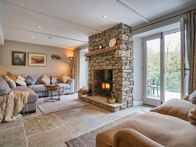 A living room with a stone fireplace sofas tables and glass doors at The Old Water Mill in Kendal