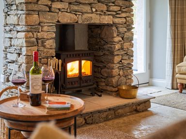 A stone fireplace with a wood burning stove and a wooden table with a bottle of wine and two glasses at The Old Water Mill in Kendal