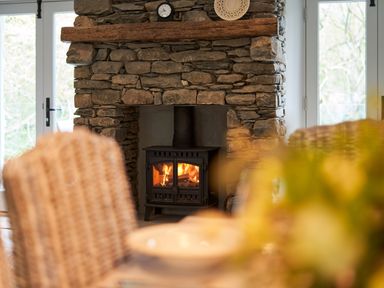 A stone fireplace with a wood-burning stove and a clock on the mantel at The Old Water Mill in Kendal