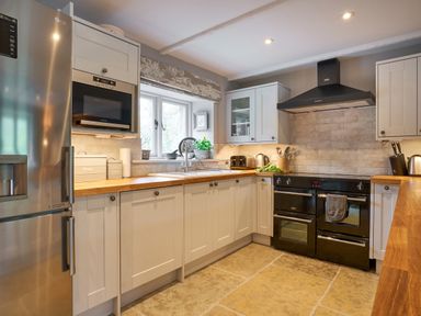 A kitchen with white cabinets wooden countertops a black oven and microwave stainless steel refrigerator and window at The Old Water Mill in Kendal