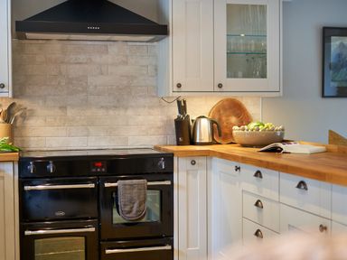 A kitchen with black oven and stove wooden countertop white cabinets and a bowl of fruit at The Old Water Mill in Kendal
