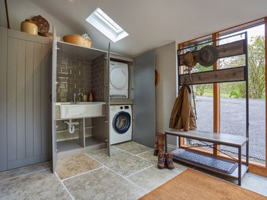 A utility room with washer and dryer in cabinets and a bench with coat rack near a large window at The Old Water Mill in Kendal