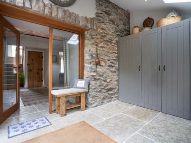 A hallway with stone walls wooden bench grey cabinets and glass doors at The Old Water Mill in Kendal
