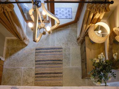An entryway with a striped rug stone floor wooden door beige curtains lamp on a wooden cabinet and a round wooden mirror at The Old Water Mill in Kendal