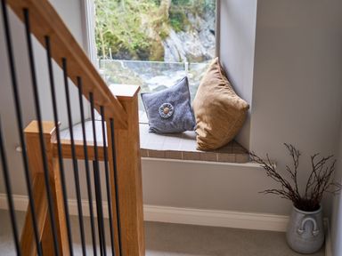 A window seat with two cushions next to a wooden staircase and a vase with branches at The Old Water Mill in Kendal