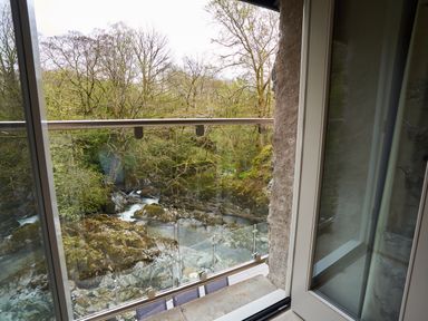 A view of a river and trees from a glass balcony door at The Old Water Mill in Kendal
