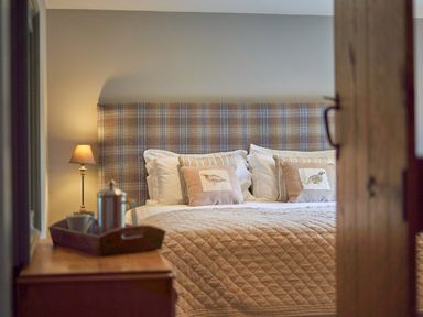 A bedroom with a bed with checkered headboard pillows lamp and a wooden dresser at The Old Water Mill in Kendal
